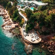 Aerial view of Four Seasons Astir Palace Hotel Athens, with modern villas, private swimming pools, and a long staircase leading to a patio with lounge chairs, next to clear, blue waters