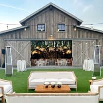 Couches are arranged on the lawn outside a barn used for a wedding reception, which is adorned with tables and flowers inside.