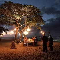 Musicians play for a table of guests enjoying dinner on the beach at sundown.