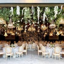Elegant wedding reception featuring tables set beneath hanging flowers and chandeliers, creating a romantic atmosphere.