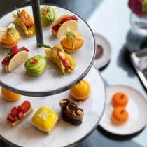 Tiered tray displaying an assortment of colourful, artfully crafted pastries and finger foods, including mini tacos, fruit tarts and bright glazed desserts.