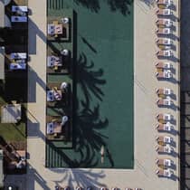 Aerial view of a man swimming in a large outdoor pool surrounded by lounge chairs and cabanas