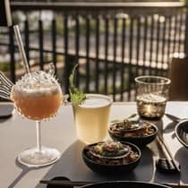 An outdoor dining table topped with colourful cocktails and small plates, overlooking a tropical mountain view