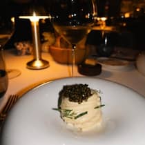Pasta with a creamy white sauce topped with fresh herbs and caviar, served at a lamplit dining table