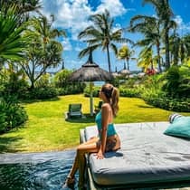 A woman lounges on a poolside daybed and looks out at a sunny ocean view