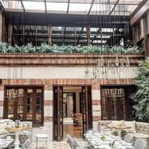 Dining tables and chairs under sunny skylight, brick indoor balcony lined with tropical plants