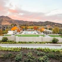 Resort pool area with surrounding greenery and buildings, set against a backdrop of rolling hills and a pink-tinged sunset sky.
