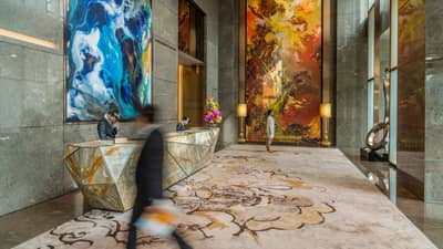 Man wearing suits walks through hotel lobby surrounded by marble, large modern art