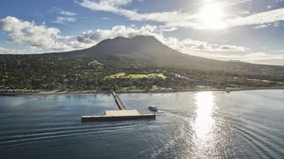 Aerial view of sun shining over Nevis mountain, lagoon with large wood bridge and dock