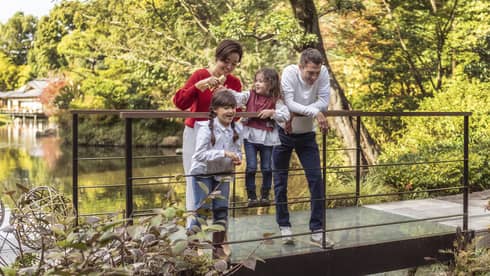 Family of four feeds koi fish from foot bridge in the Shakusui-en pond garden