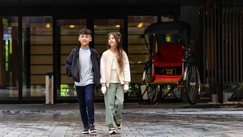 Two children smiles as they walk outside of a hotel entrance