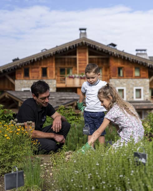 Man kneeling in meadow with two children with chalet in backdrop