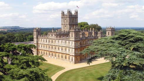 View over rolling green hills, trees to large Highclere castle building