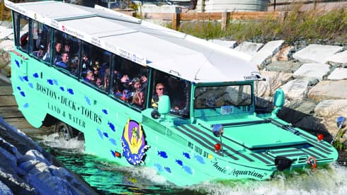 Green Boston Duck Tour bus with excited tourists in windows drives into the water