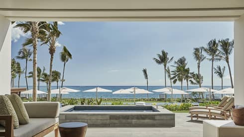 Pacific Suite's luxurious beachfront patio with a comfortable seating area, a private pool and sun loungers facing the ocean, framed by palm trees and umbrellas under a clear sky