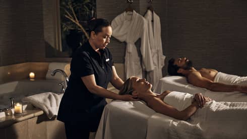 Two guests laying on massage tables in a room with a spa tub.
