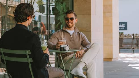 Two guests sitting at an outside dining table and holding their drinks