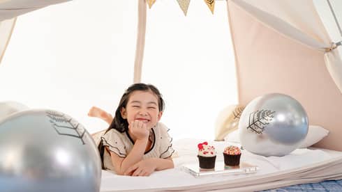 Smiling young girl in in-room kids? tent with gold and silver balloons and cupcakes