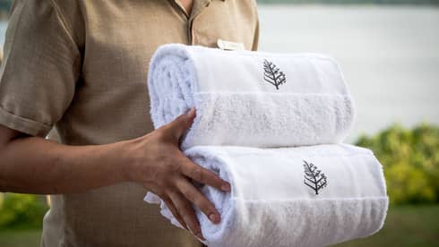 Close-up of hotel service staff carrying two rolled white towels with Four Seasons logo