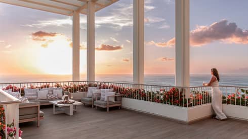 Woman gazes out to sunset view over the ocean from expansive terrace
