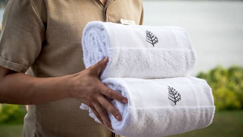 Close-up of hotel service staff carrying two rolled white towels with Four Seasons logo
