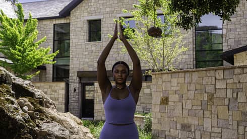 Guest wearing a purple workout set and doing yoga outside.