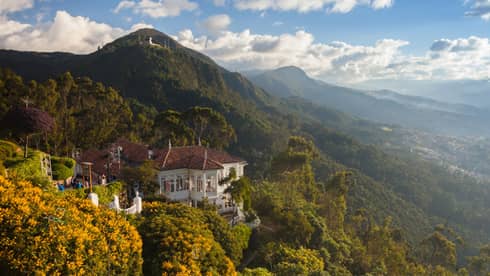 Aerial view of colonial-style white building tucked high on lush green mountain that stretches to horizon, blue sky
