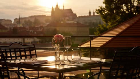 Terrace dining setup at sunset with view of Prague Castle in backdrop