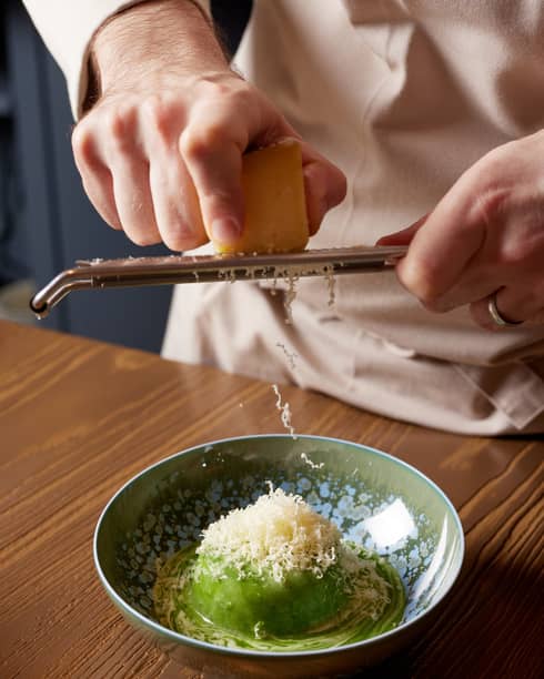 Chef grates Parmesan cheese over dish