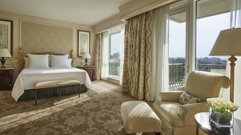 Deluxe Room bed, cream-coloured armchair beside sunny floor-to-ceiling patio door and window