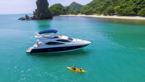 Two people in yellow kayak in front of large white yacht by island in blue ocean