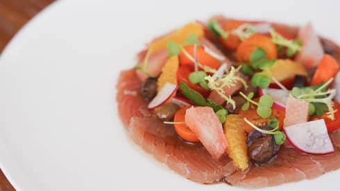 A white plate holds slices of reddish-pink fish topped with colorful garnishes.