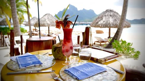 Fruity cocktail with tropical flower garnish on patio dining table by Bora Bora lagoon