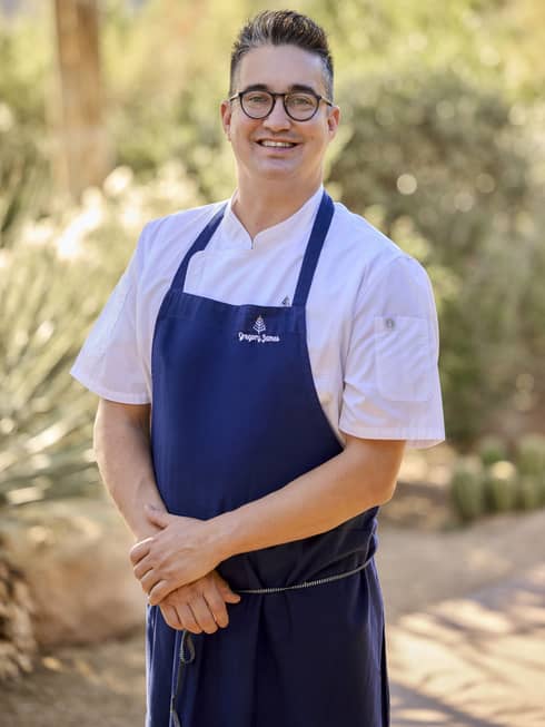 A chef poses wearing a blue apron.