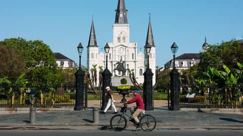 A person riding a bike in front of a large gated building.