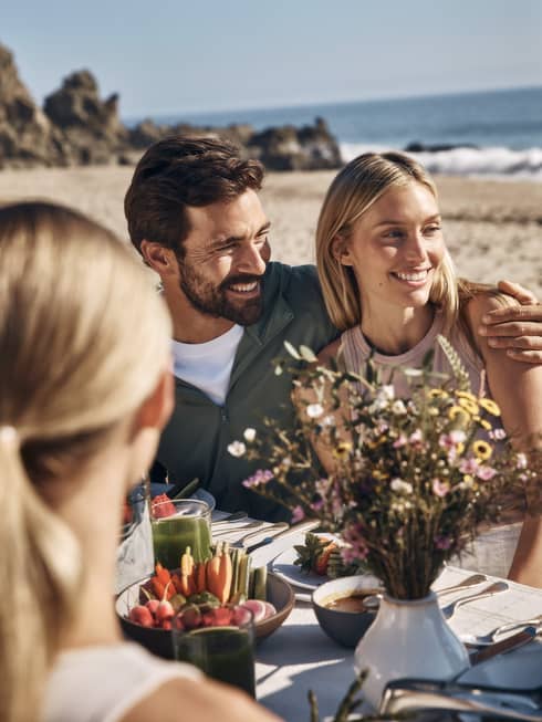 Two guests sitting at an outdoor dining table together with the ocean in the background.