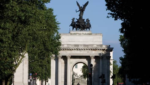 View through trees to Wellington Arch monument and statue against blue sky