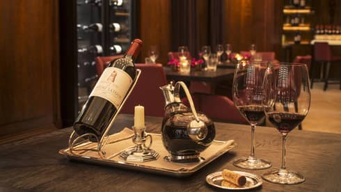 A bottle of red wine, a decanter and two glasses in a dimly lit restaurant.