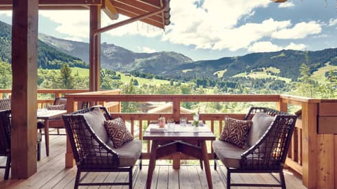 Two cushioned benches with table in middle on wooden terrace with mountain views