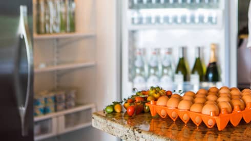 Smiling man holds green bottle in front of open fridge, fresh eggs on counter