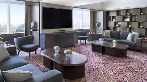Living room with burgundy patterned carpet, two grey sofas, two coffee tables and TV