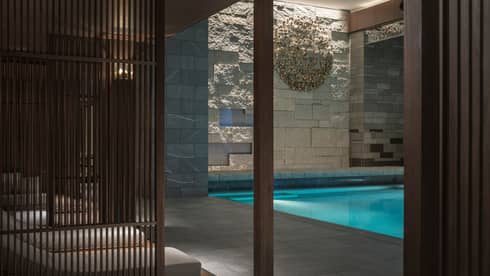 Lounge chairs behind wood wall, by indoor swimming pool under granite rock wall