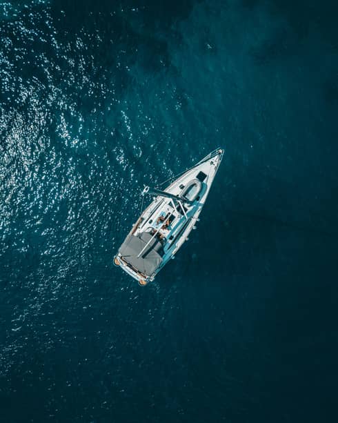 Distant aerial view of two guests sunbathing on a yacht surrounded by shimmering midnight-blue water.