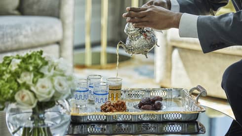 Table with roses, staff pouring tea into decorative glass cups on tray with dates