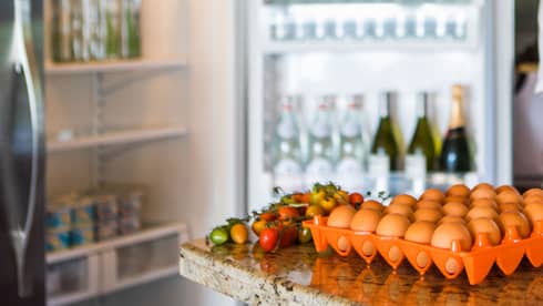 Smiling man holds green bottle in front of open fridge, fresh eggs on counter