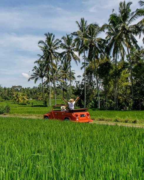 Couple driving orange Volkswagen through Bali countryside