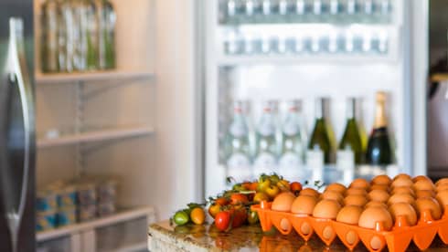 Smiling man holds green bottle in front of open fridge, fresh eggs on counter