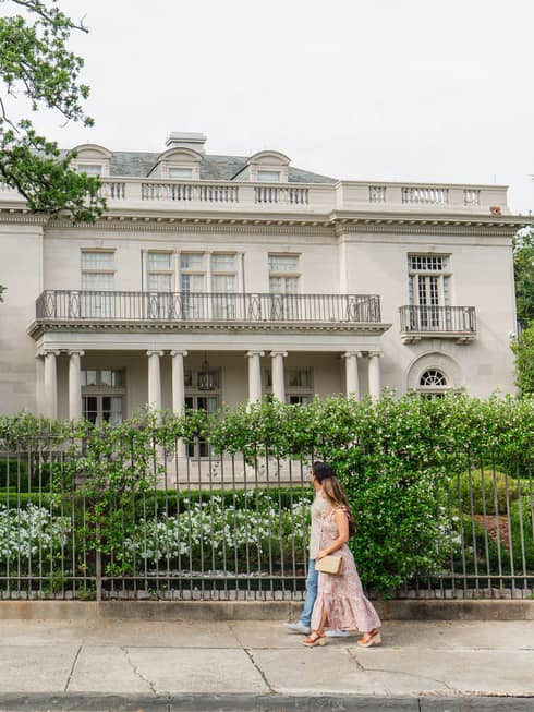 Two guests walking on the sidewalk in front of a fence and house.