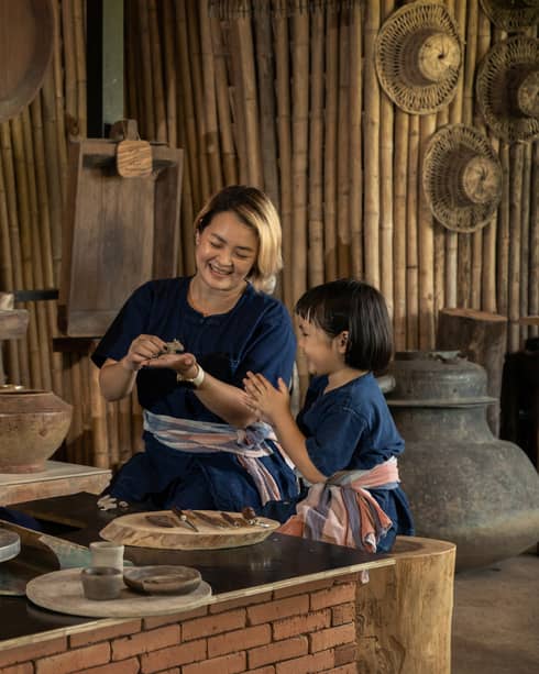 A potter teaching a woman and a child to shape clay in a rustic pottery workshop, surrounded by traditional tools and pottery.