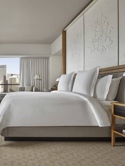 Suite with white king-size bed, flat screen TV, emerald green armchair and floor-to-ceiling windows